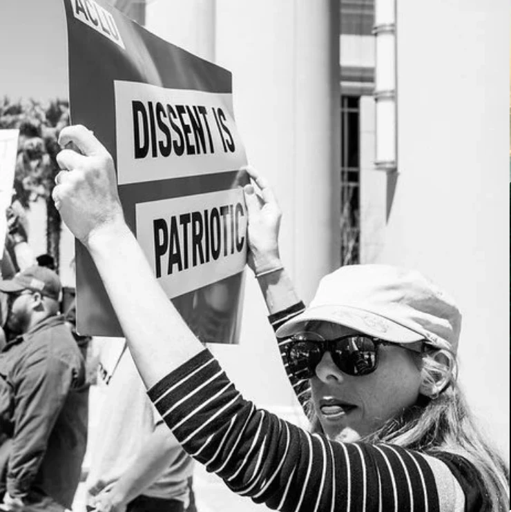 Black-and-white photograph of a protester holding a sign that reads Dissent is patriotic.